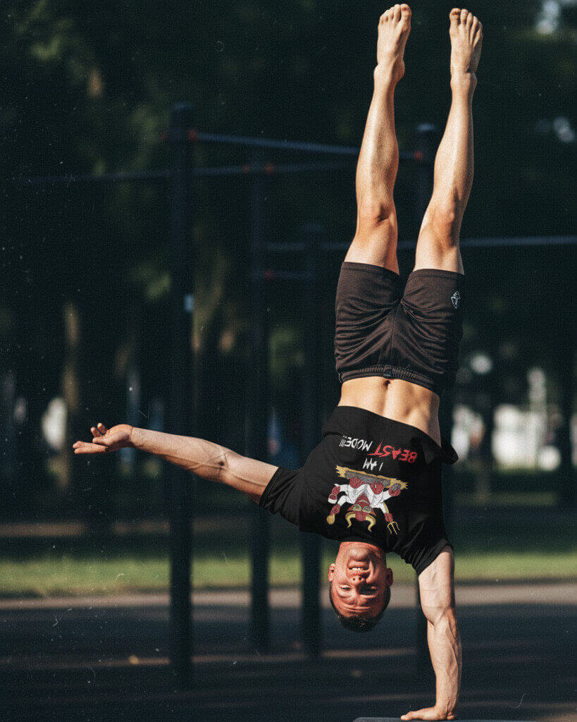 Athlete performing a one-handed handstand at an outdoor gym, wearing the Sovereign Emblem "Beast Mode" t-shirt.