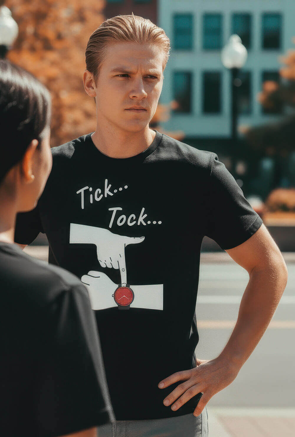 Model with an impatient expression on a city street, wearing the Sovereign Emblem "Tick... Tock..." t-shirt.